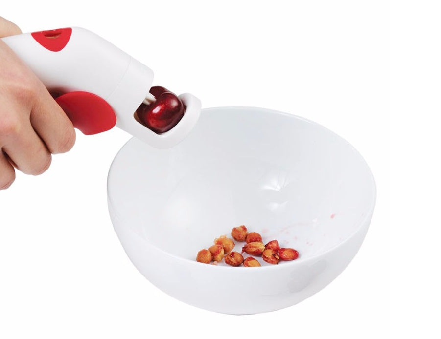 Using handheld cherry pitter to remove pits into bowl